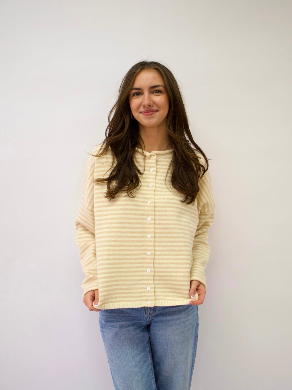 Woman wearing a light yellow striped shirt and blue jeans against a white background