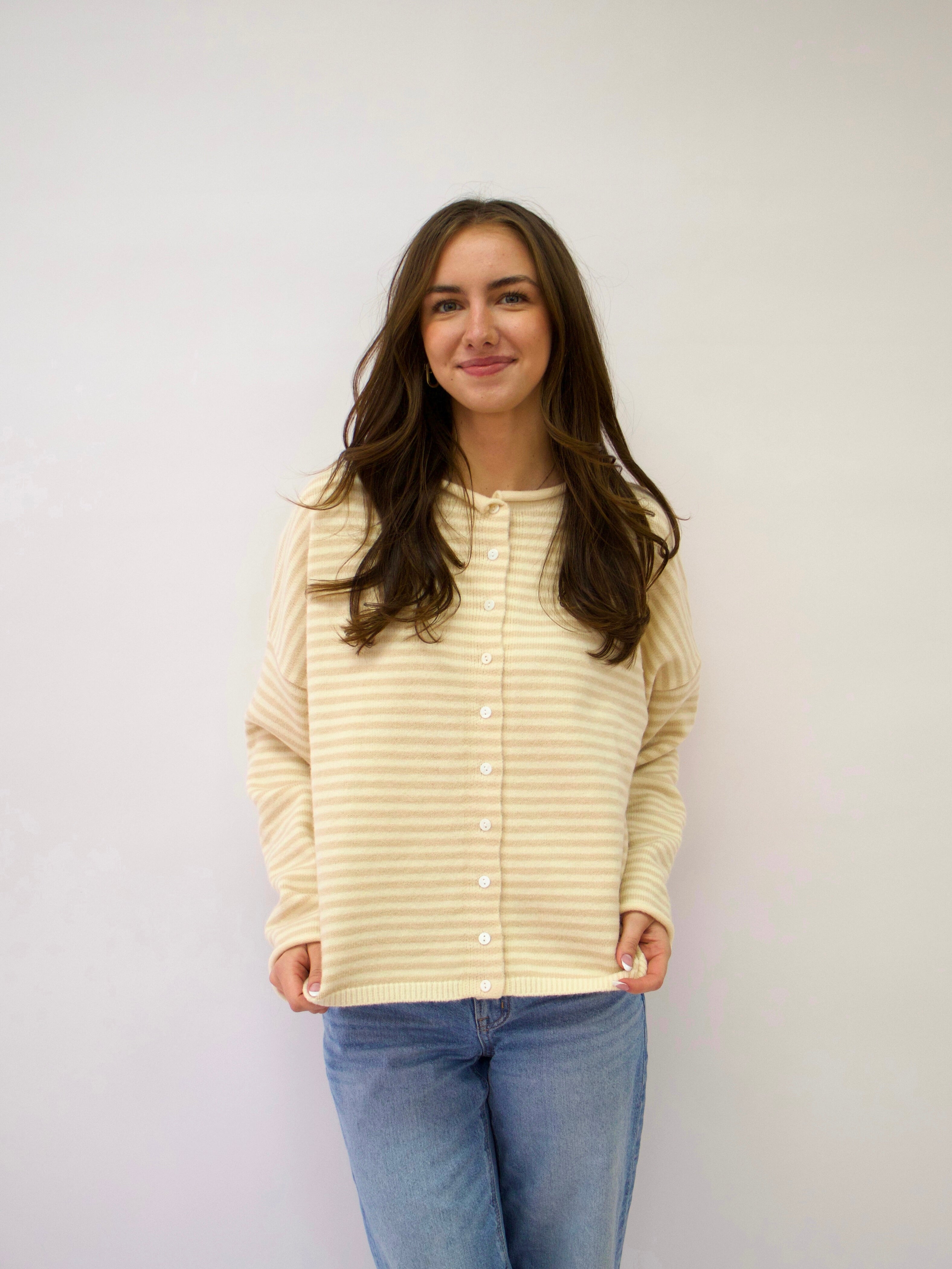 Woman wearing a light yellow striped shirt and blue jeans against a white background